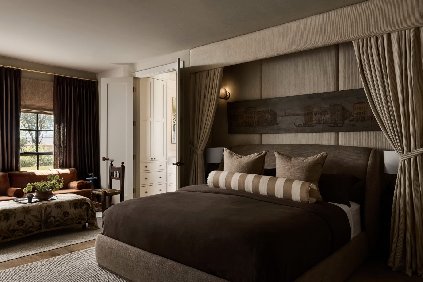 Primary bedroom with upholstered wall panels, a draped canopy alcove and an antique Venetian panel over the bed