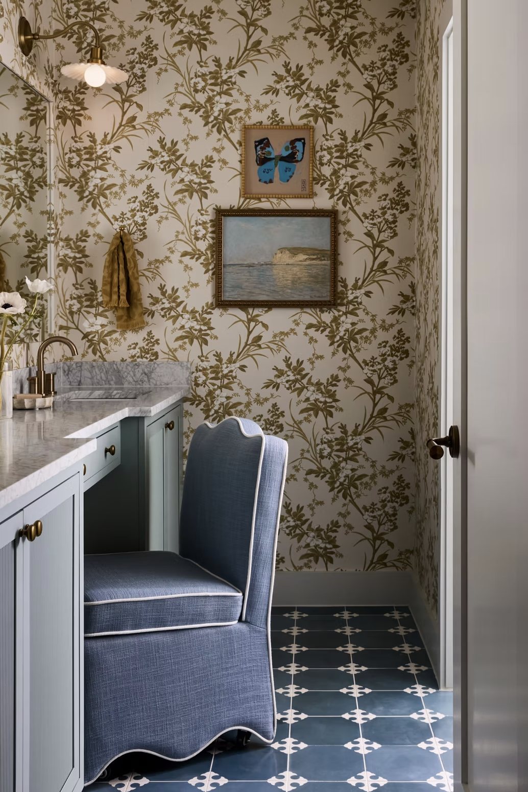 Bath with botanical wallpaper, a blue fluted vanity, scalloped skirted chair and patterned blue tile