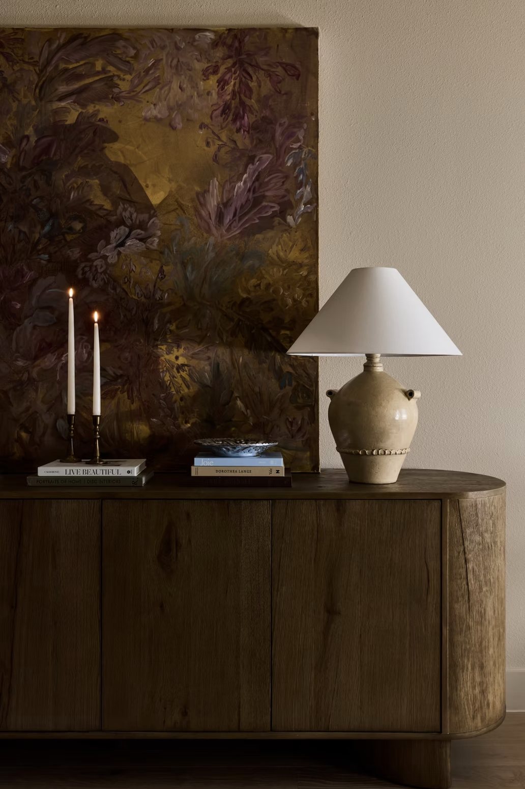 Rounded oak sideboard with a stoneware lamp, candles and an oversized floral painting