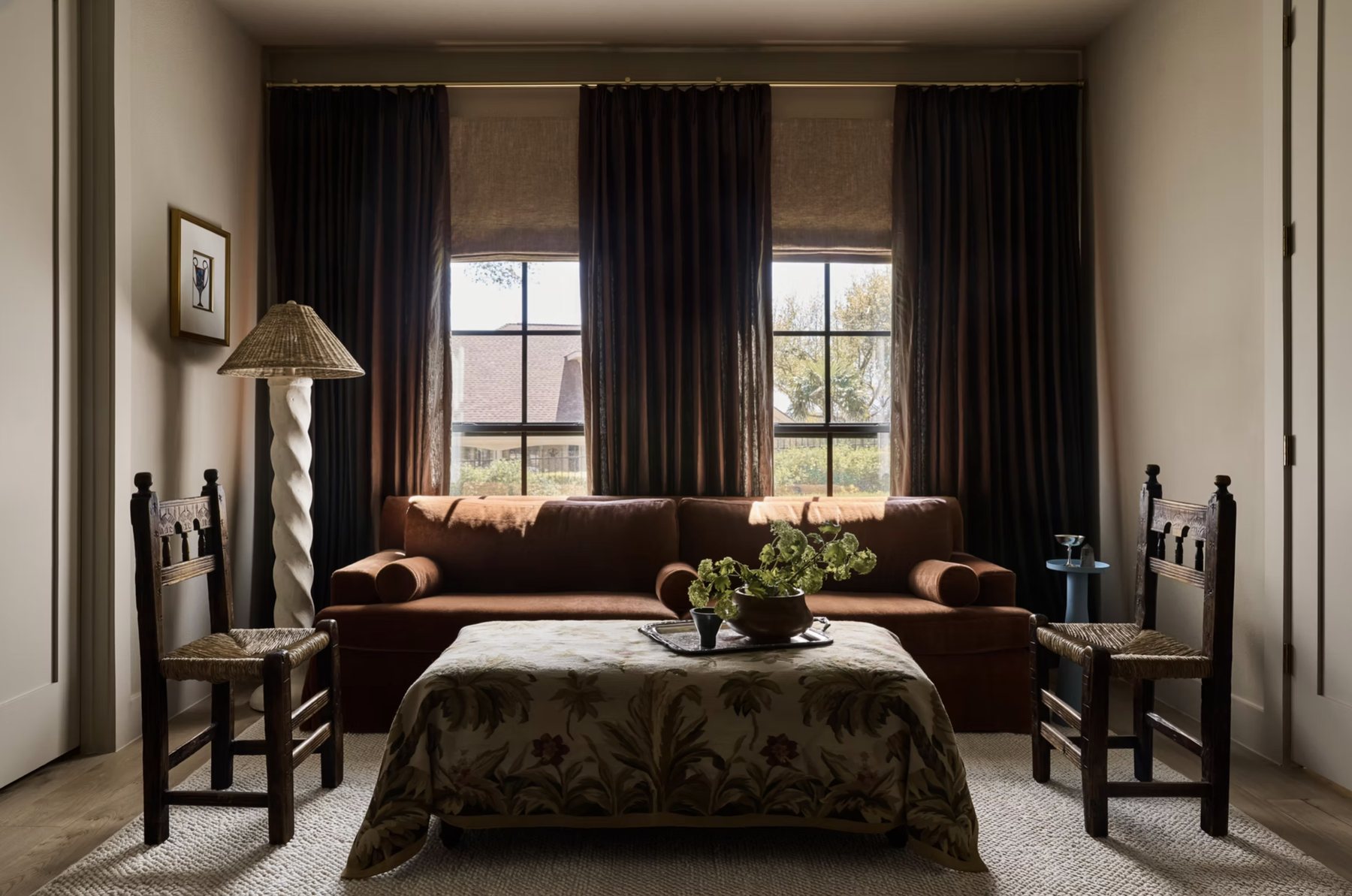 Bedroom sitting area with a rust velvet sofa, tapestry ottoman, rush chairs and chocolate drapery