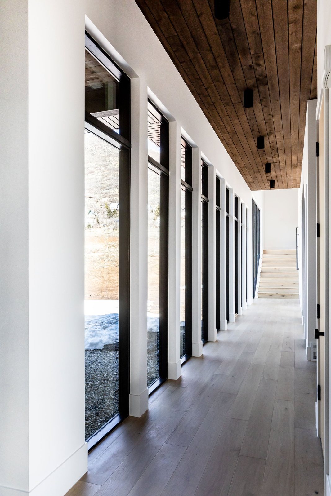 Gallery hallway lined with tall black-framed windows under a wood ceiling