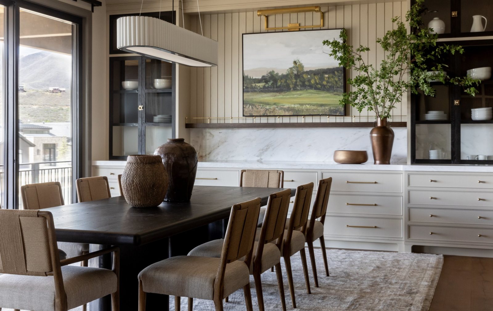 Mountainside dining room with black oak table, rush-back chairs, marble buffet and landscape painting
