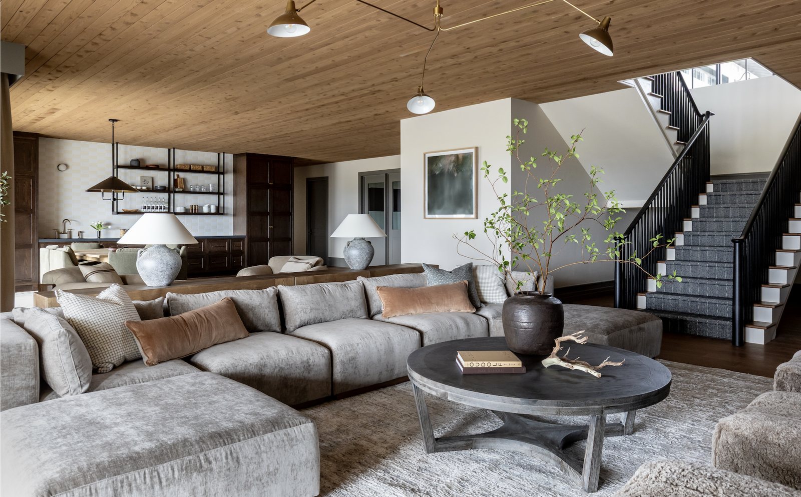 Family room with velvet sectional, plank wood ceiling and black stair rail